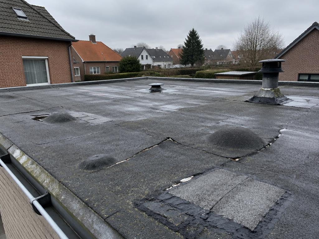 Gebarsten en opgelapt bitumen plat dak vóór de vernieuwing door Merchiers Dak en Woningrenovatie