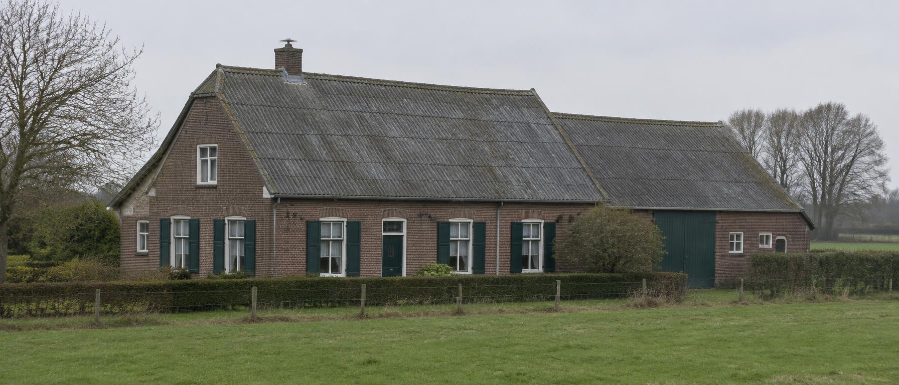 Oud grijs asbestleiendak op een Vlaamse hoeve, gezien van een afstand in rustig daglicht